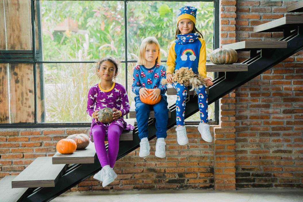 Three children sitting on a stairs wearing bright organic cotton clothing